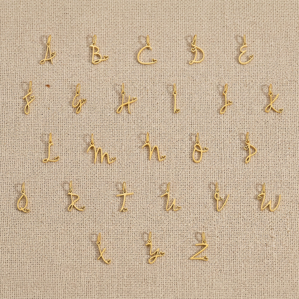 Set of gold letter charms on a beige fabric background