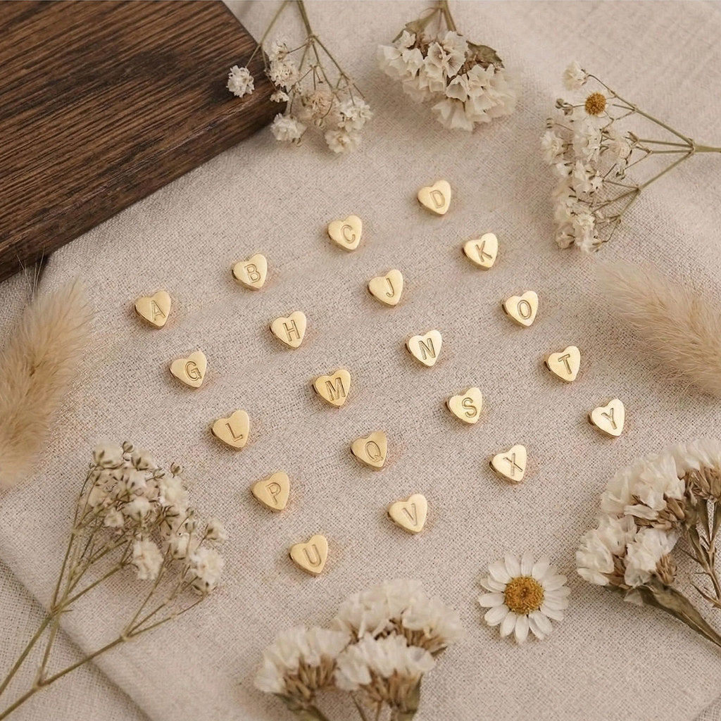 Gold heart-shaped letter tokens on a textured surface with dried flowers