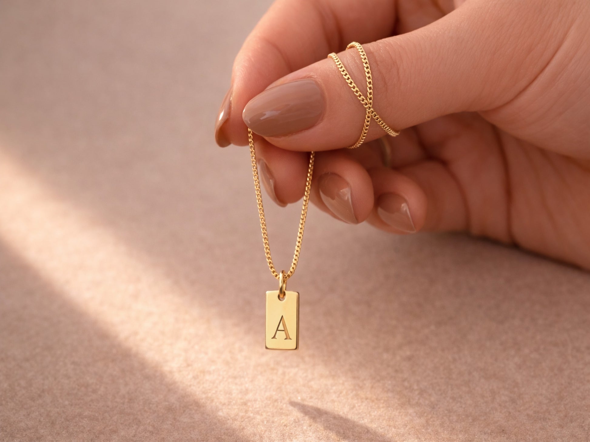 Close-up of engraved initial tag pendant in gold - Calioras