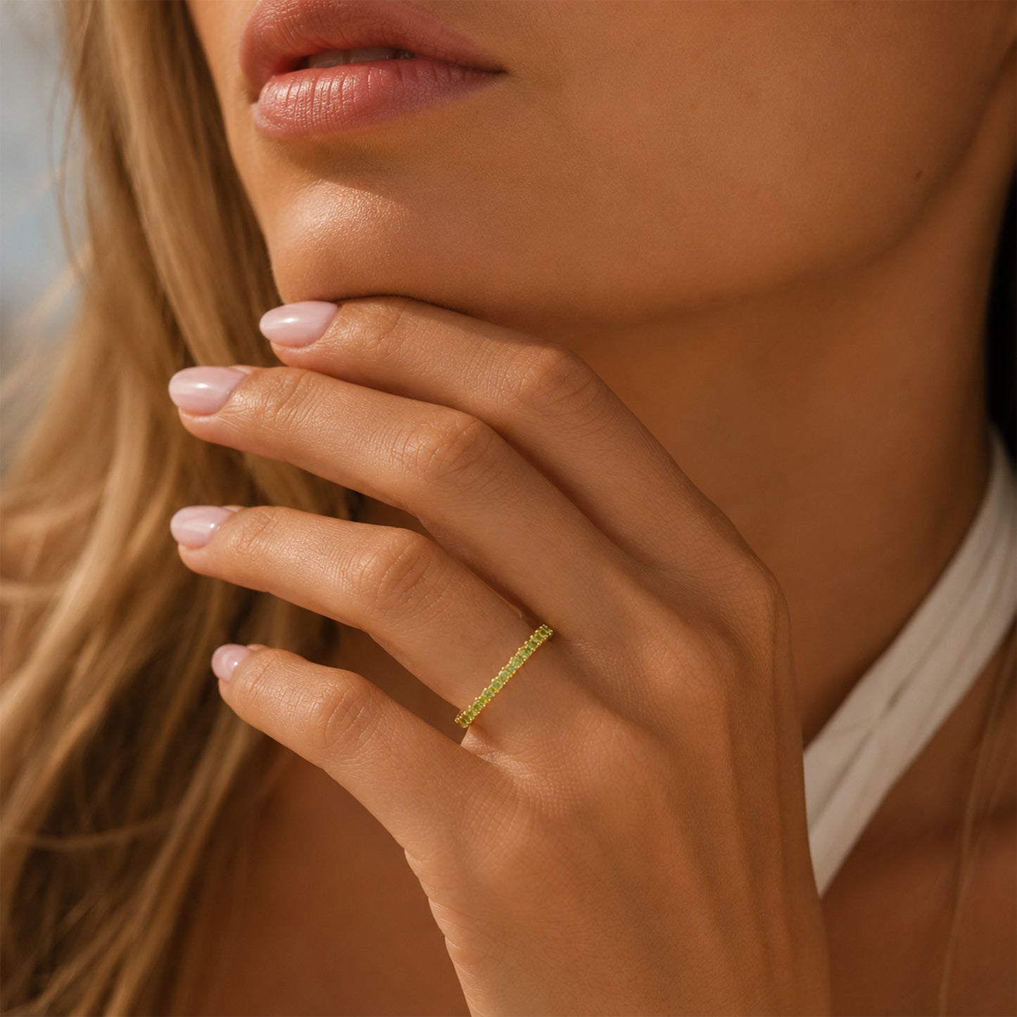 A close-up lifestyle shot of a woman wearing a delicate yellow gold ring set with small green gemstones on her ring finger.