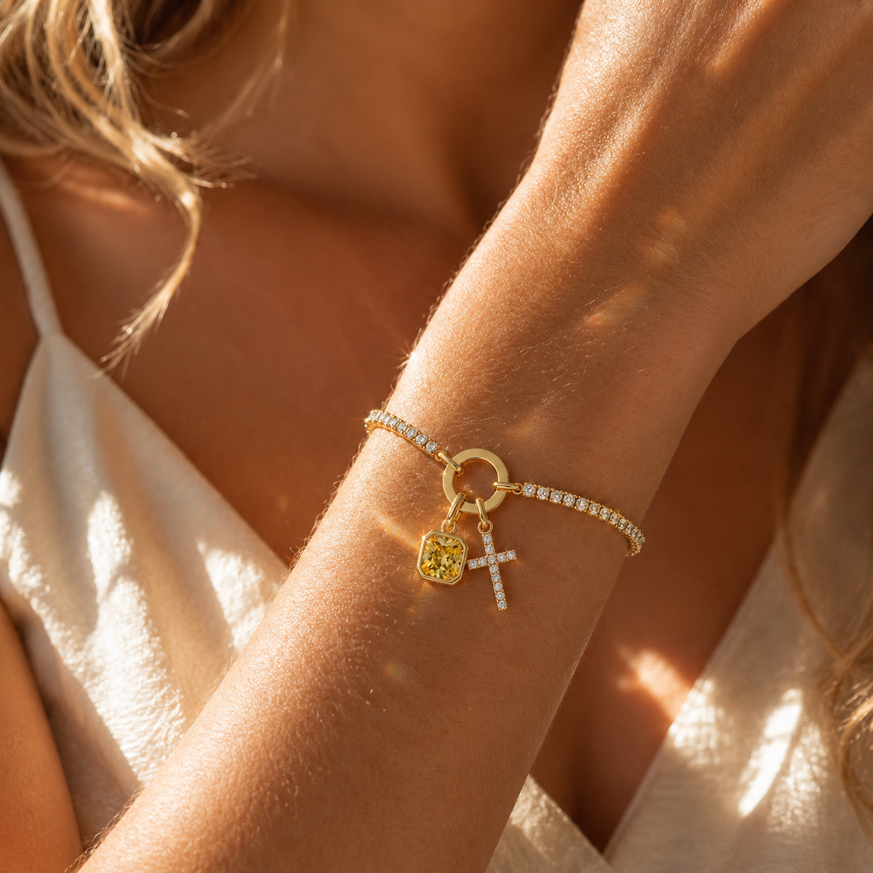 Woman wearing gold tennis cross bracelet with yellow birthstone in sunlight