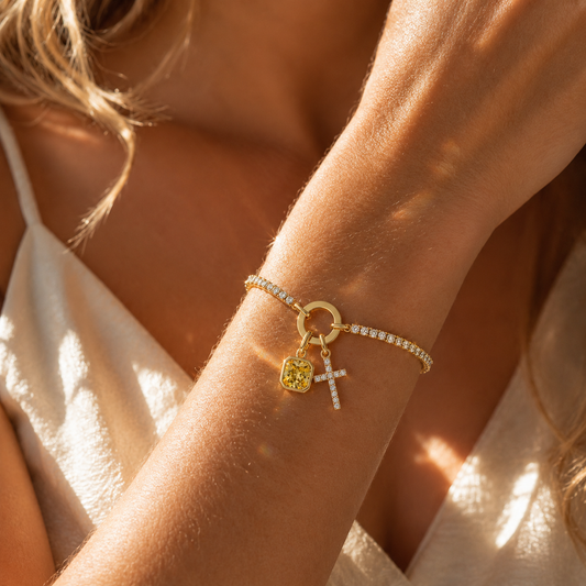Woman wearing gold tennis cross bracelet with yellow birthstone in sunlight