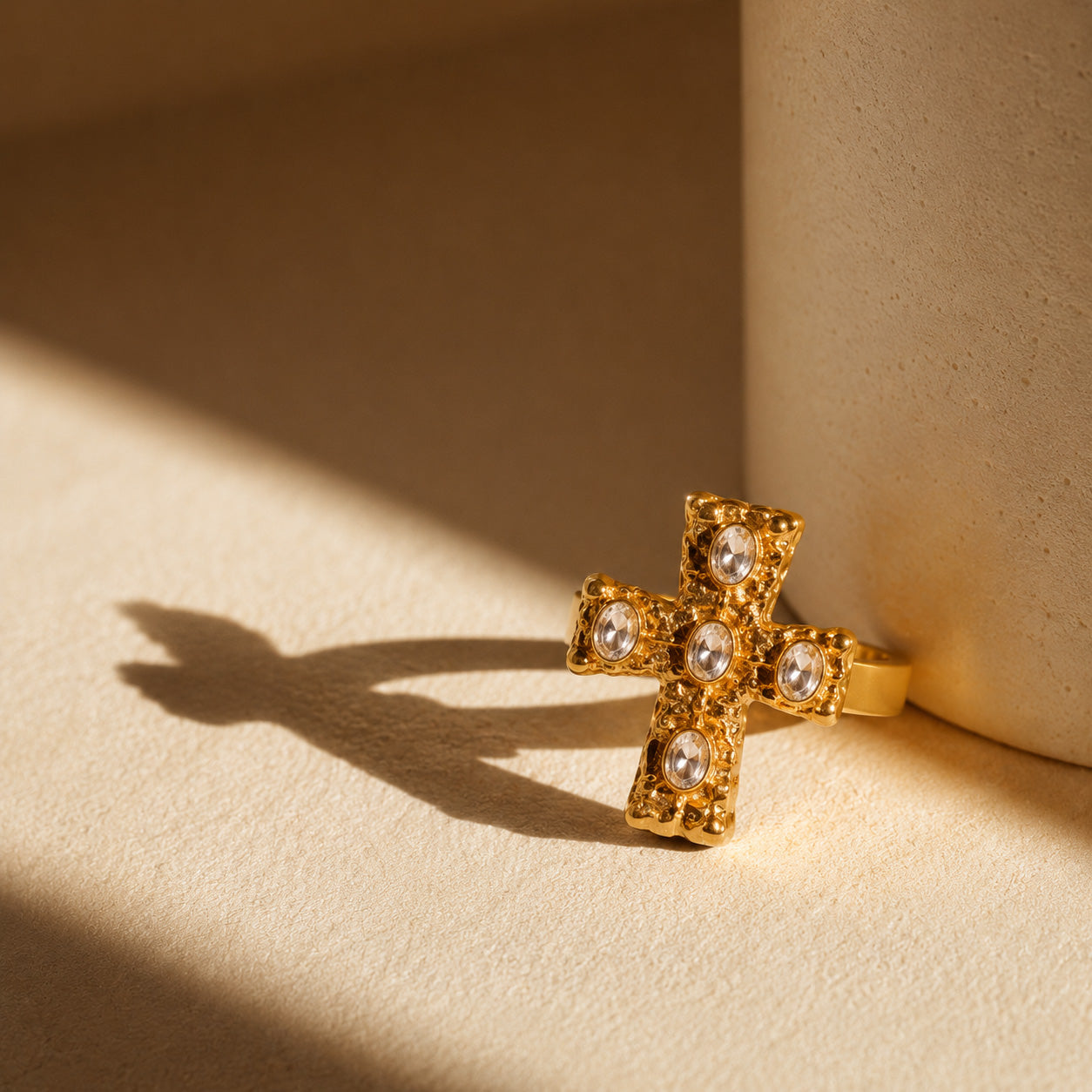 Baroque cross ring resting on cream still life with sunlight shadow