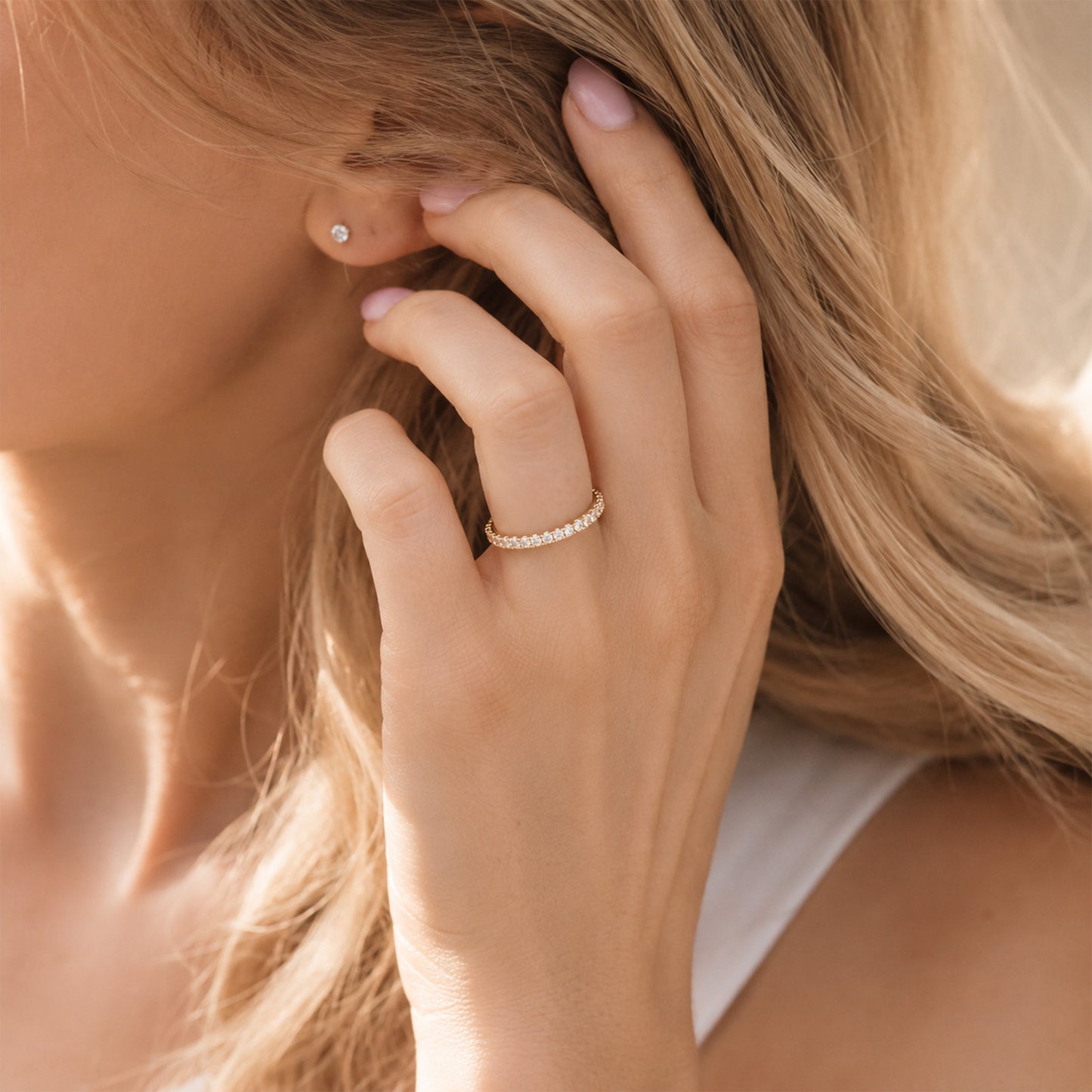 Woman wearing gold birthstone eternity ring on finger, dainty pave CZ band closeup