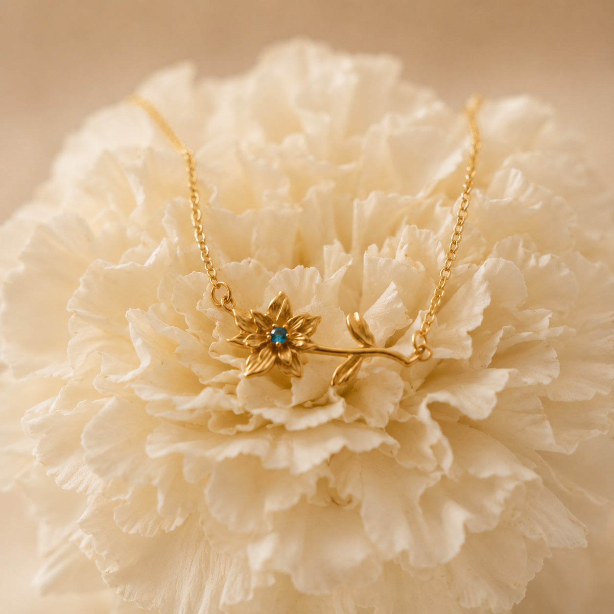 Gold birthstone flower necklace styled beside a real white bloom