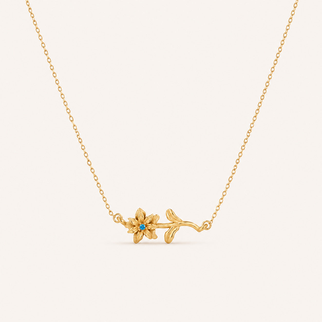 Birthstone flower necklace in 18K gold with birthstone flower pendant on cream background
