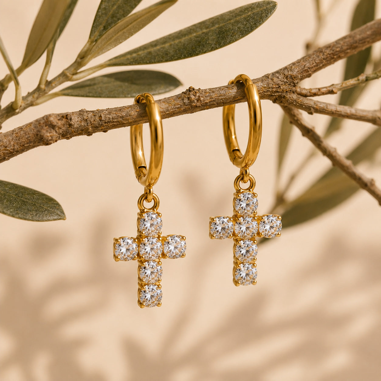Pair of gold crystal cross drop hoop earrings on olive branch still life