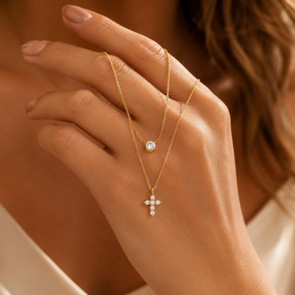 Gold double layer necklace draped over finger showing crystal solitaire and petal cross