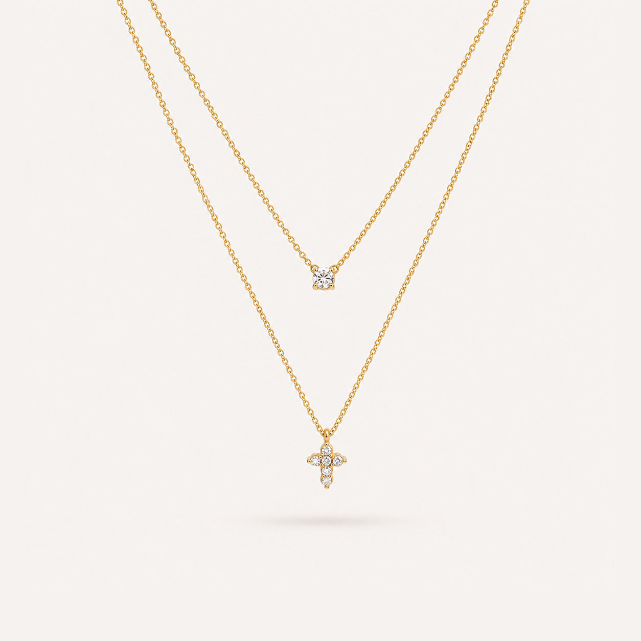 Double layer mini cross necklace in 18K gold with crystal solitaire and petal cross on cream background