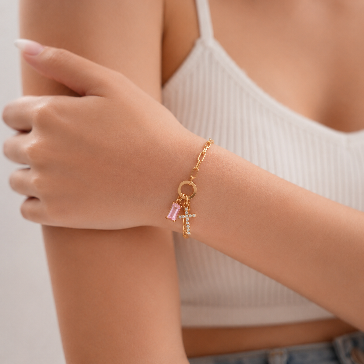 Woman wearing gold paperclip birthstone cross bracelet with pink birthstone