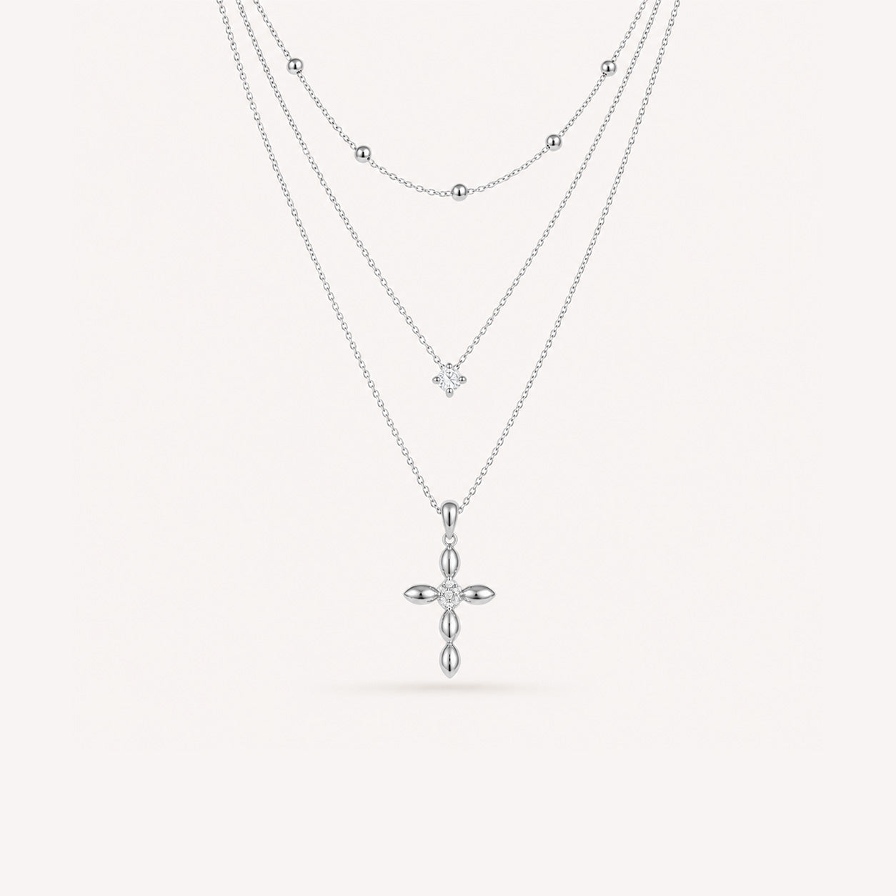 Layered petal cross necklace set in silver on cream background