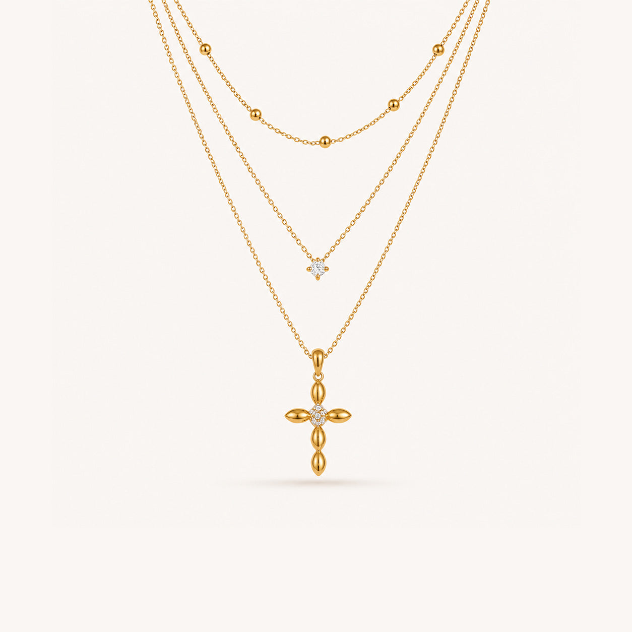 Layered petal cross necklace set in 18K gold with three strands on cream background