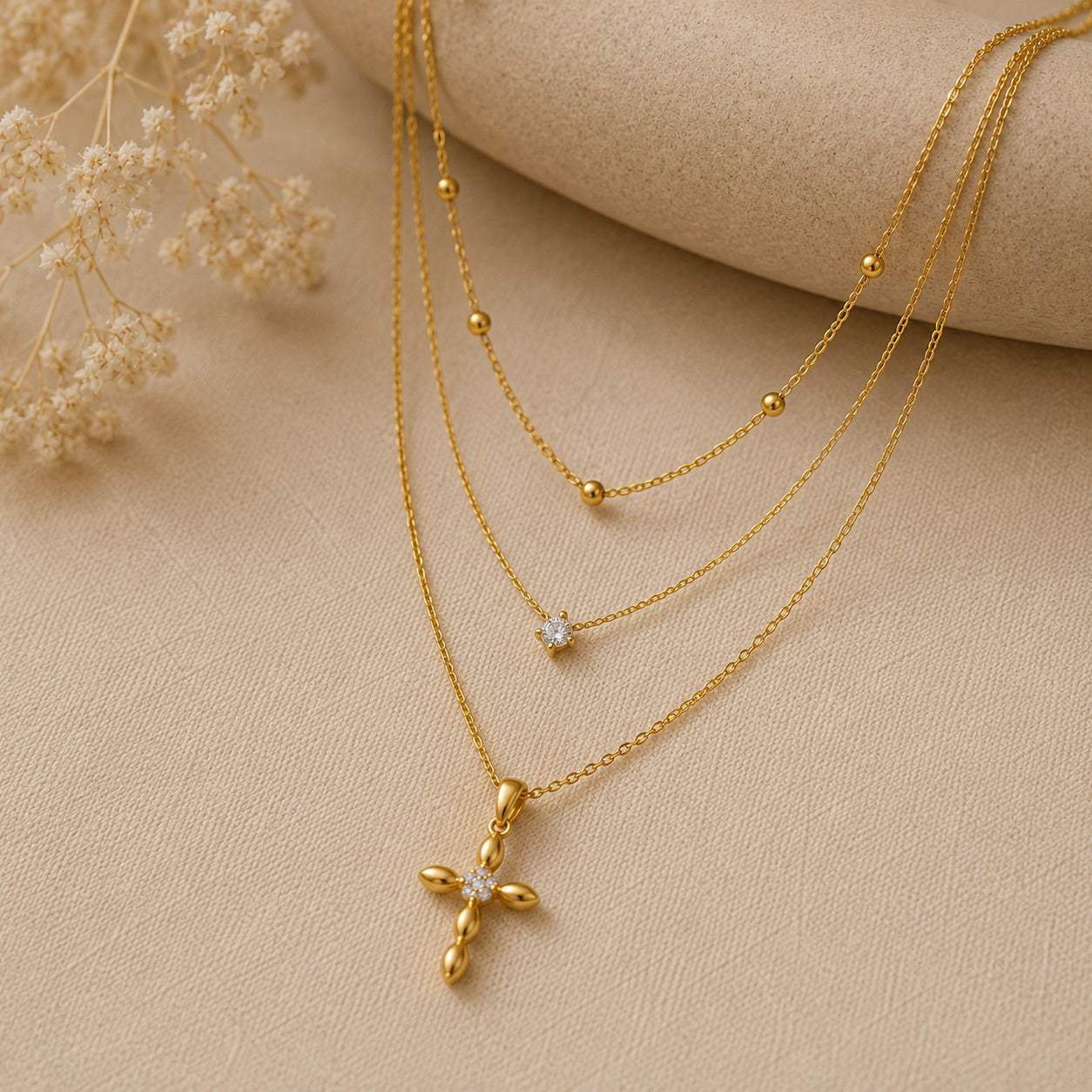 Layered petal cross necklace set draped over cream ceramic still life