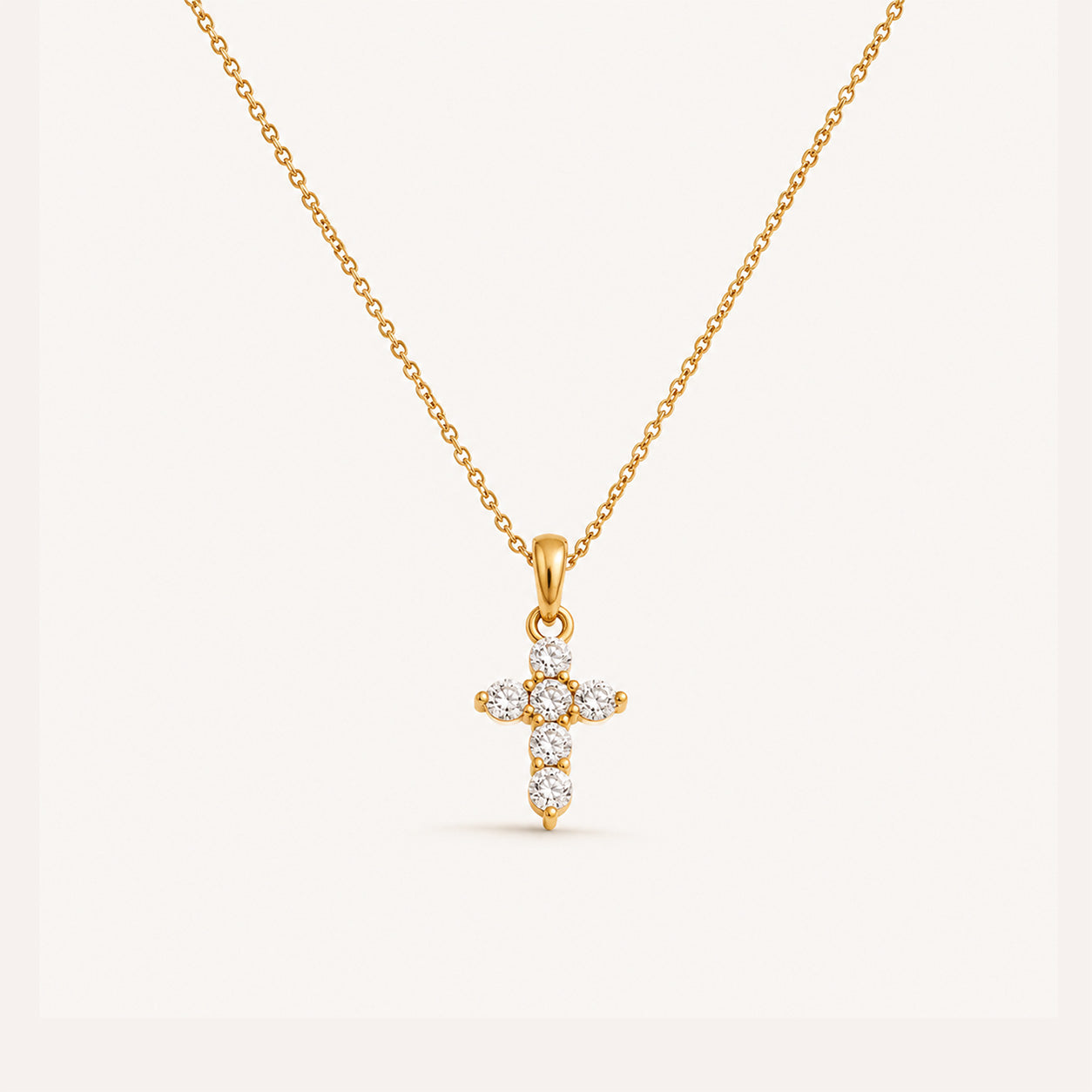 Mini crystal cross necklace in 18K gold on cream background