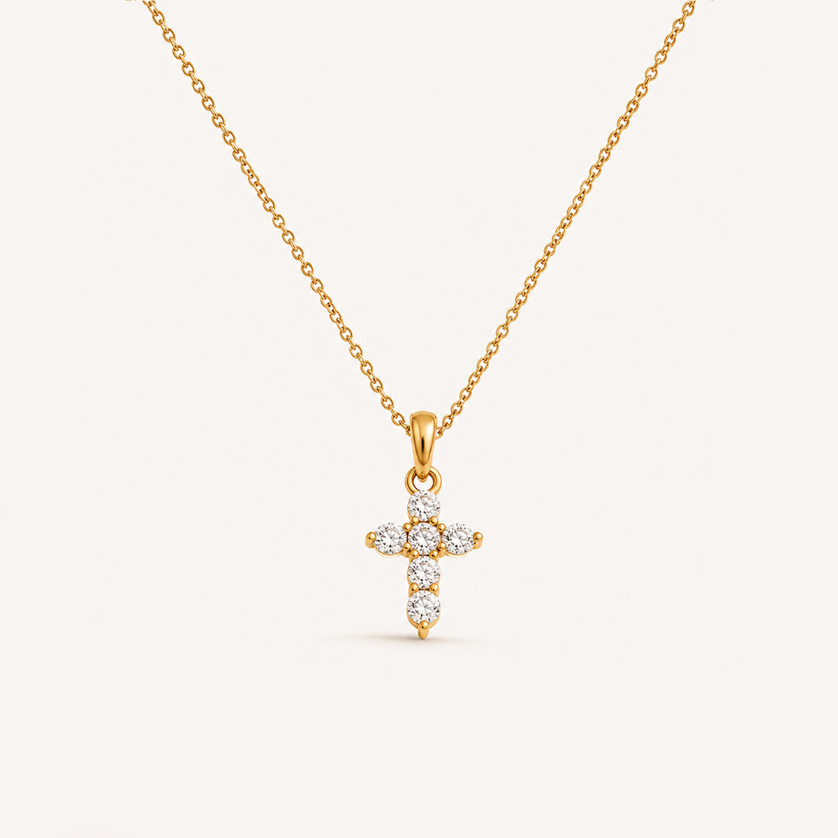 
Mini crystal cross necklace in 18K gold on cream background
