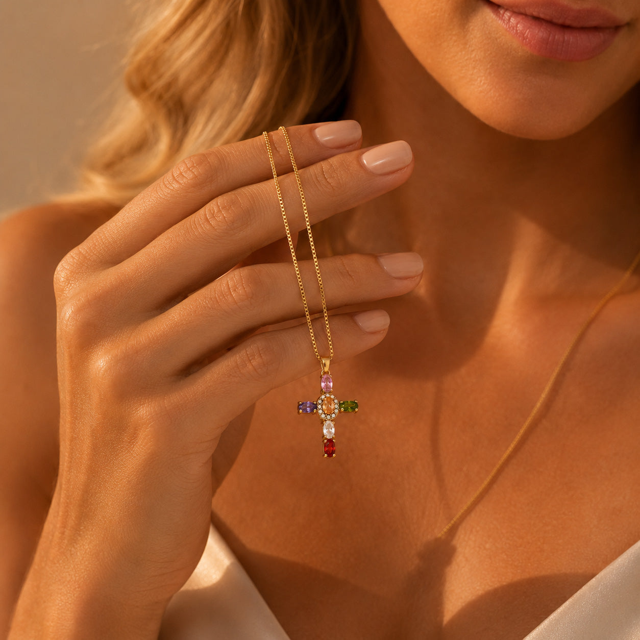 Gold gemstone halo cross necklace draped over finger showing rainbow crystal cross