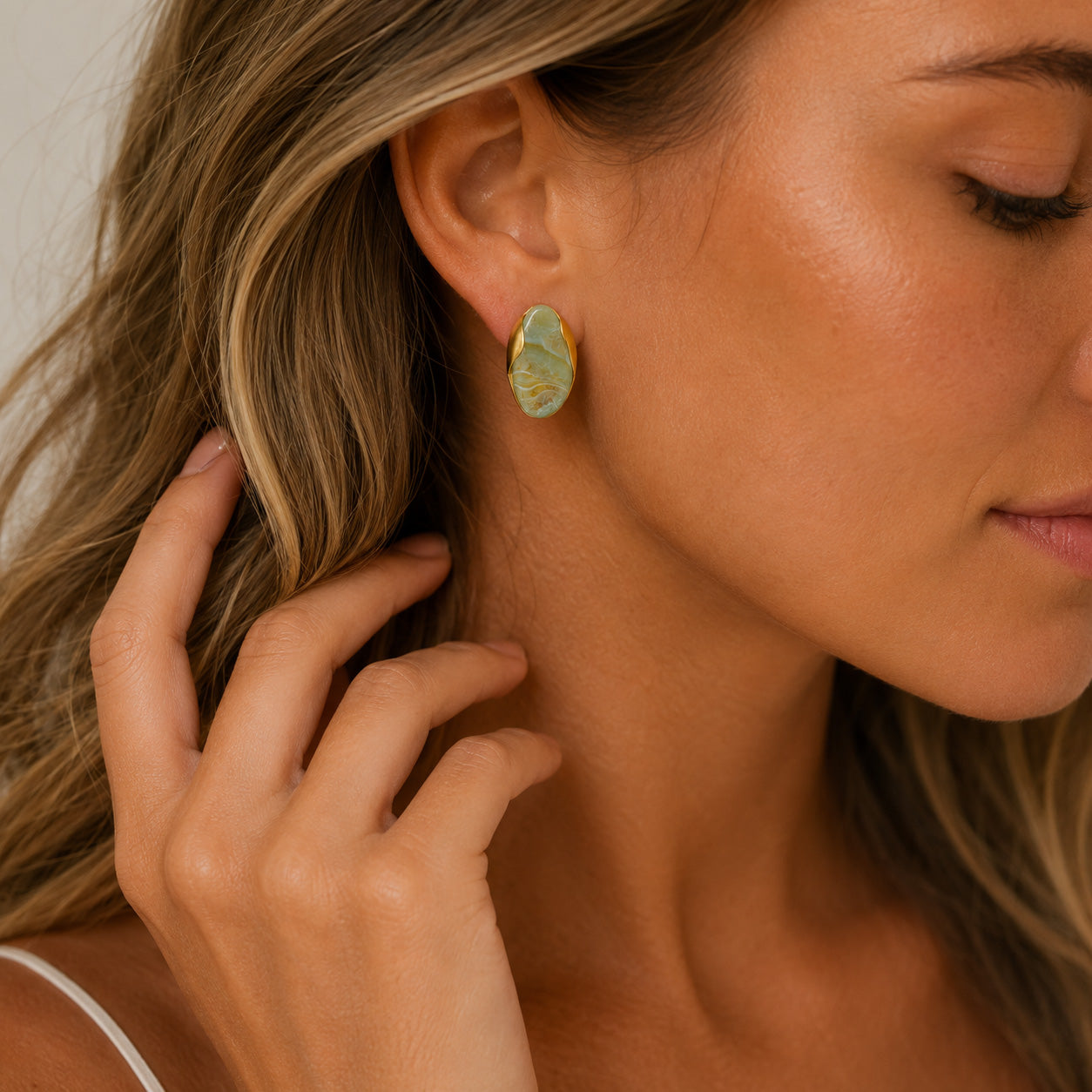 Hand tucking hair behind ear showing gold oval birthstone stud earring