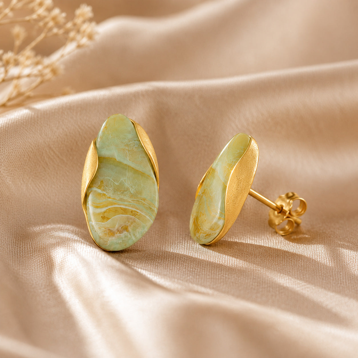 Pair of gold oval birthstone stud earrings on cream ceramic still life