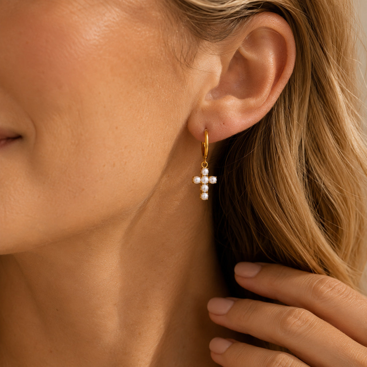 Close up of gold hoop with pearl drop and cross charm on ear