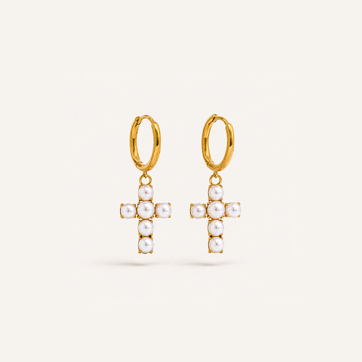 Pearl cross drop hoop earrings in 18K gold on cream background