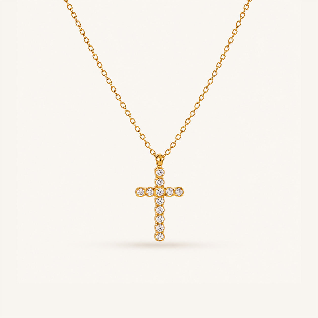 Round crystal cross necklace in 18K gold on cream background