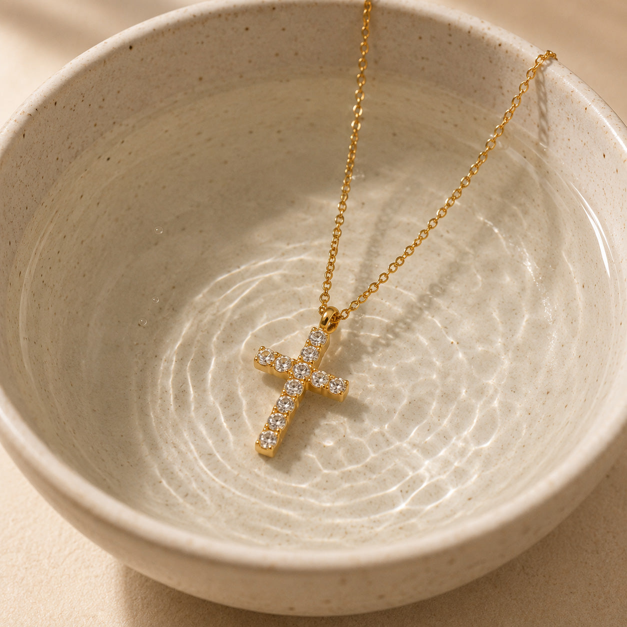 Round crystal cross necklace draped over cream ceramic still life