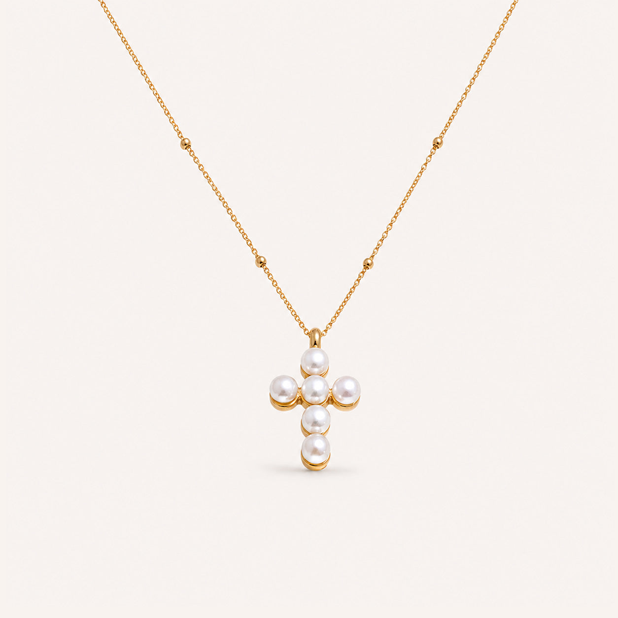 Satellite pearl cross necklace in 18K gold on cream background