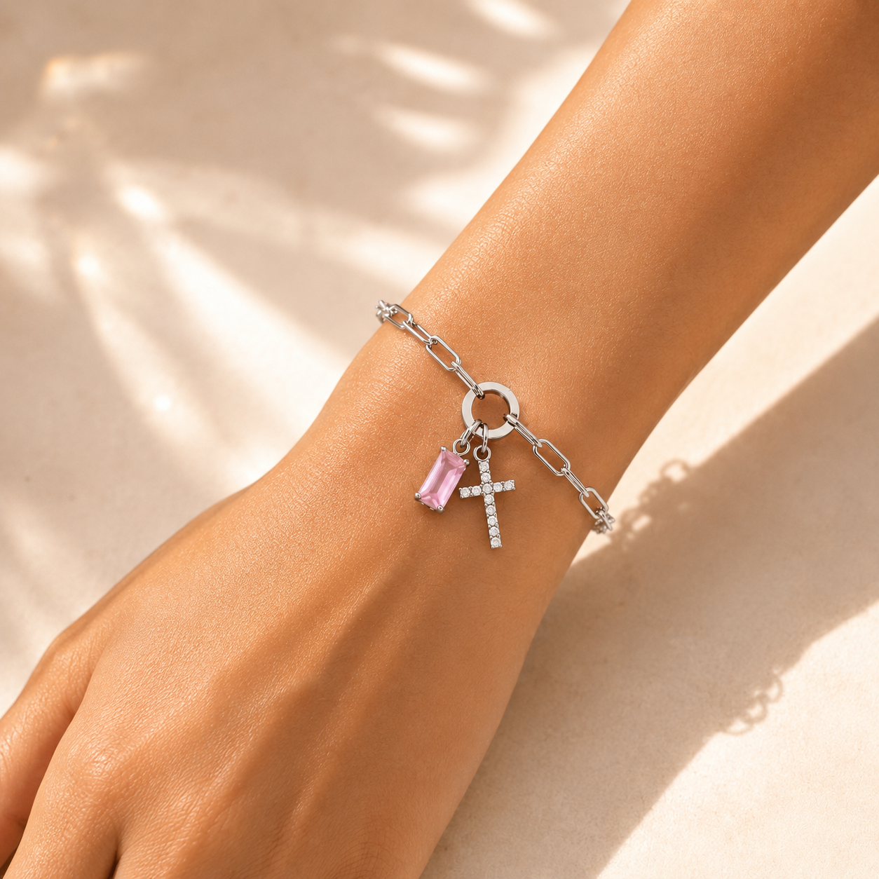 Woman wearing silver paperclip birthstone cross bracelet with pink birthstone in sunlight