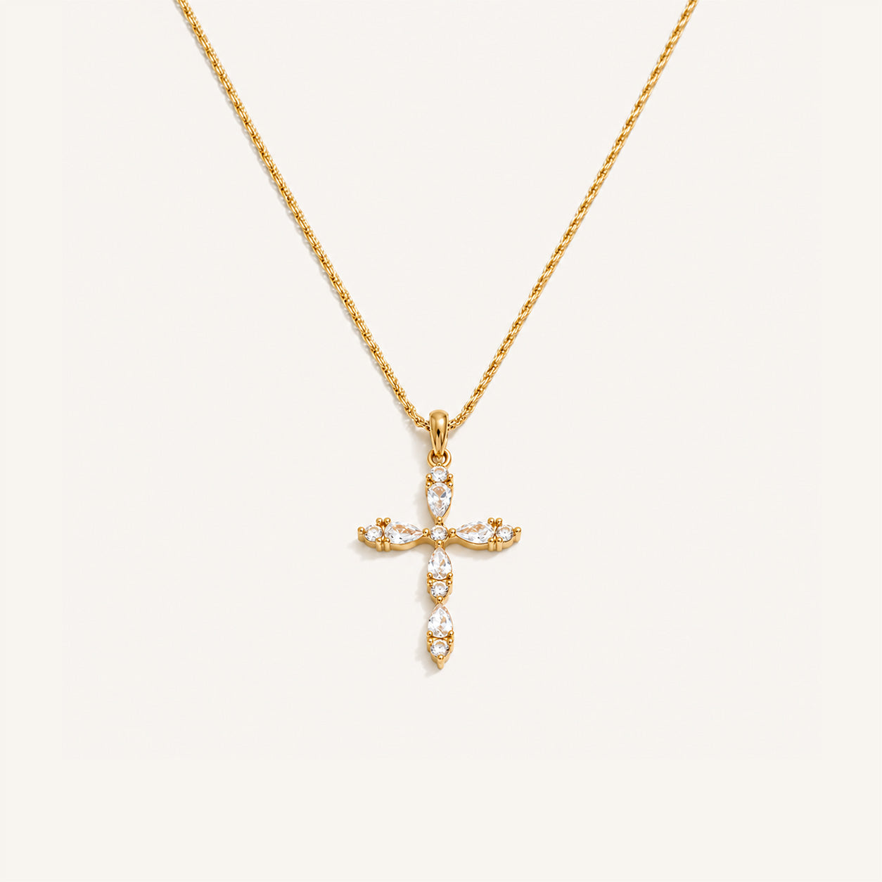 Teardrop crystal cross necklace in 18K gold on cream background