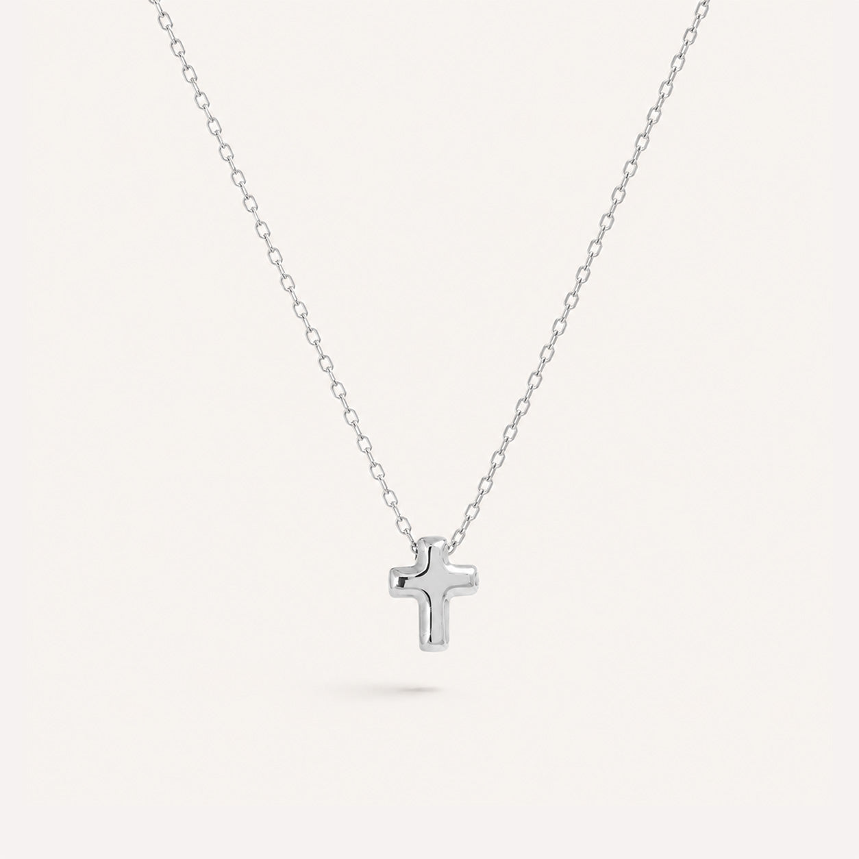 Tiny puffed plain cross necklace in silver on cream background