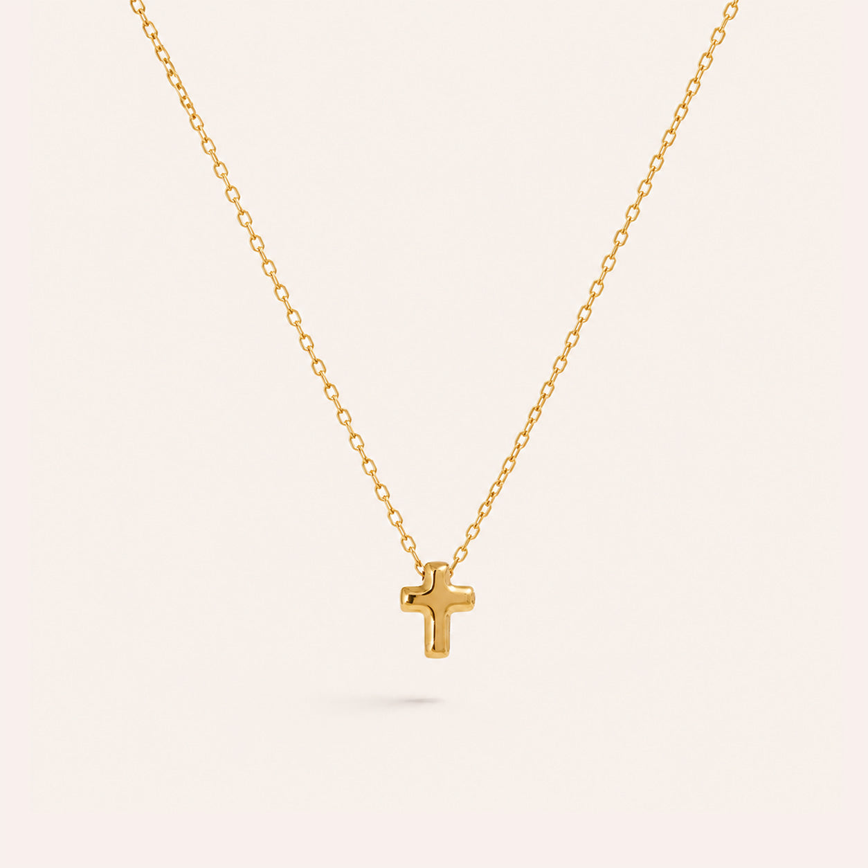 Tiny gold cross necklace with small puffed plain cross in 18K gold on cream background
