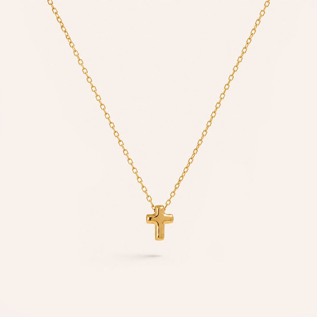 Tiny gold cross necklace with small puffed plain cross in 18K gold on cream background