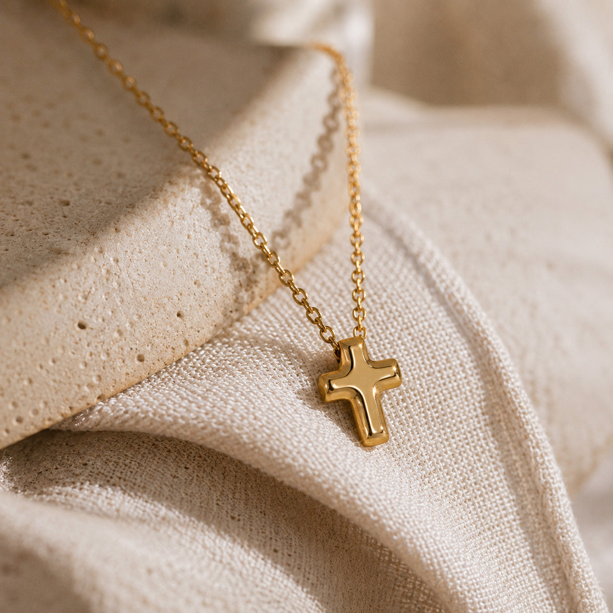 Tiny gold cross necklace draped over cream ceramic still life
