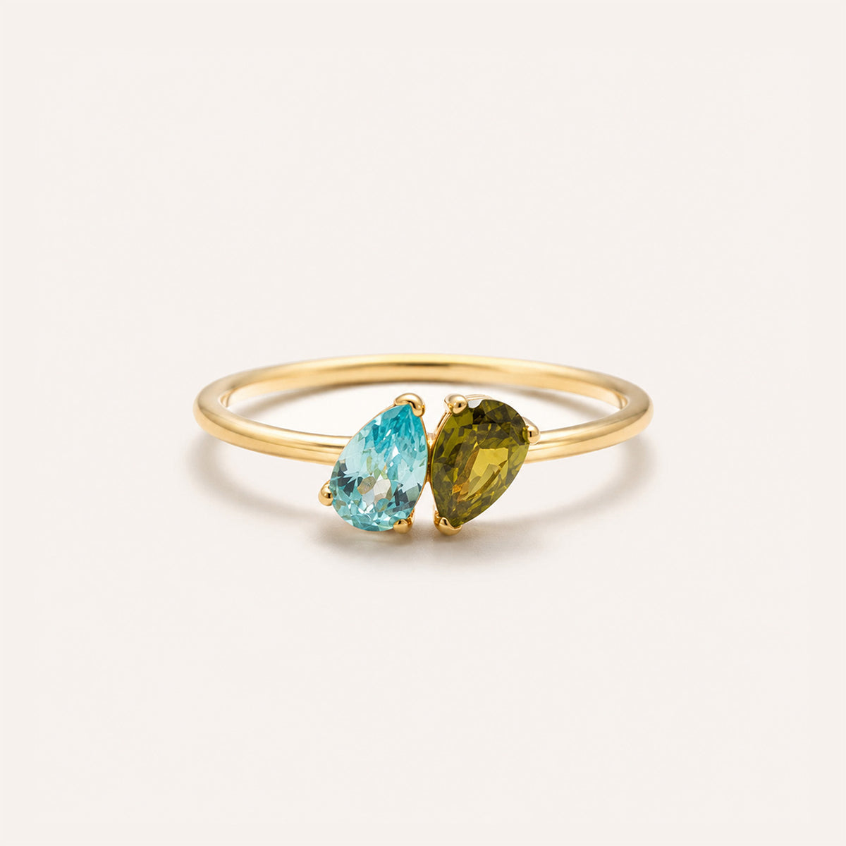 Toi et moi birthstone ring in 18K gold with aquamarine and peridot pear stones on cream background