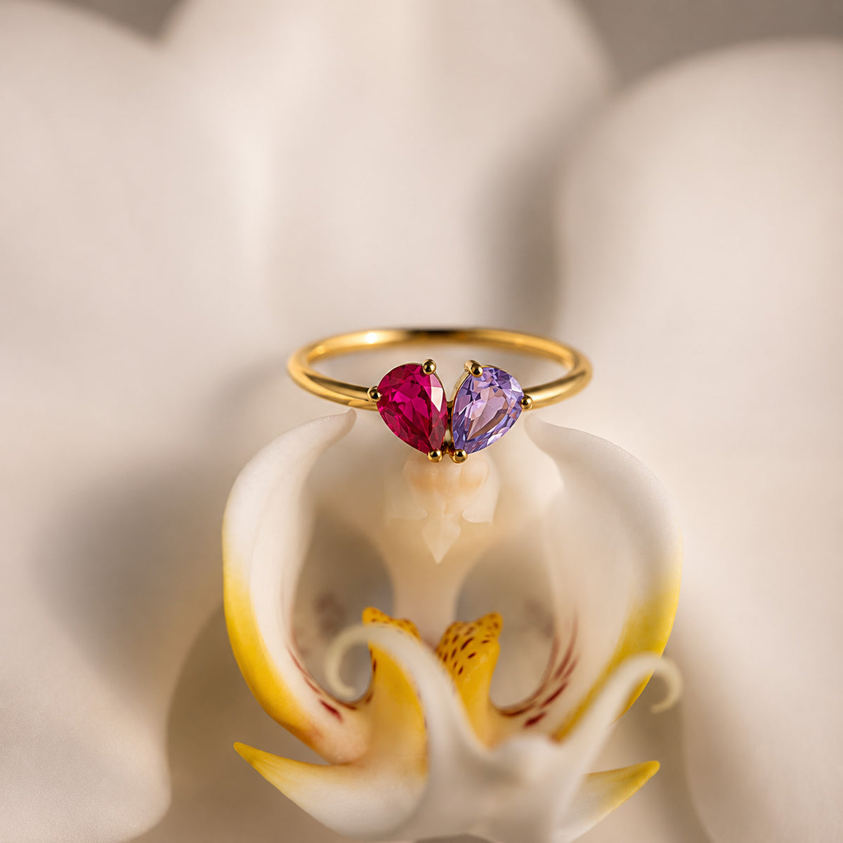 Gold toi et moi teardrop birthstone ring resting on a white orchid still life