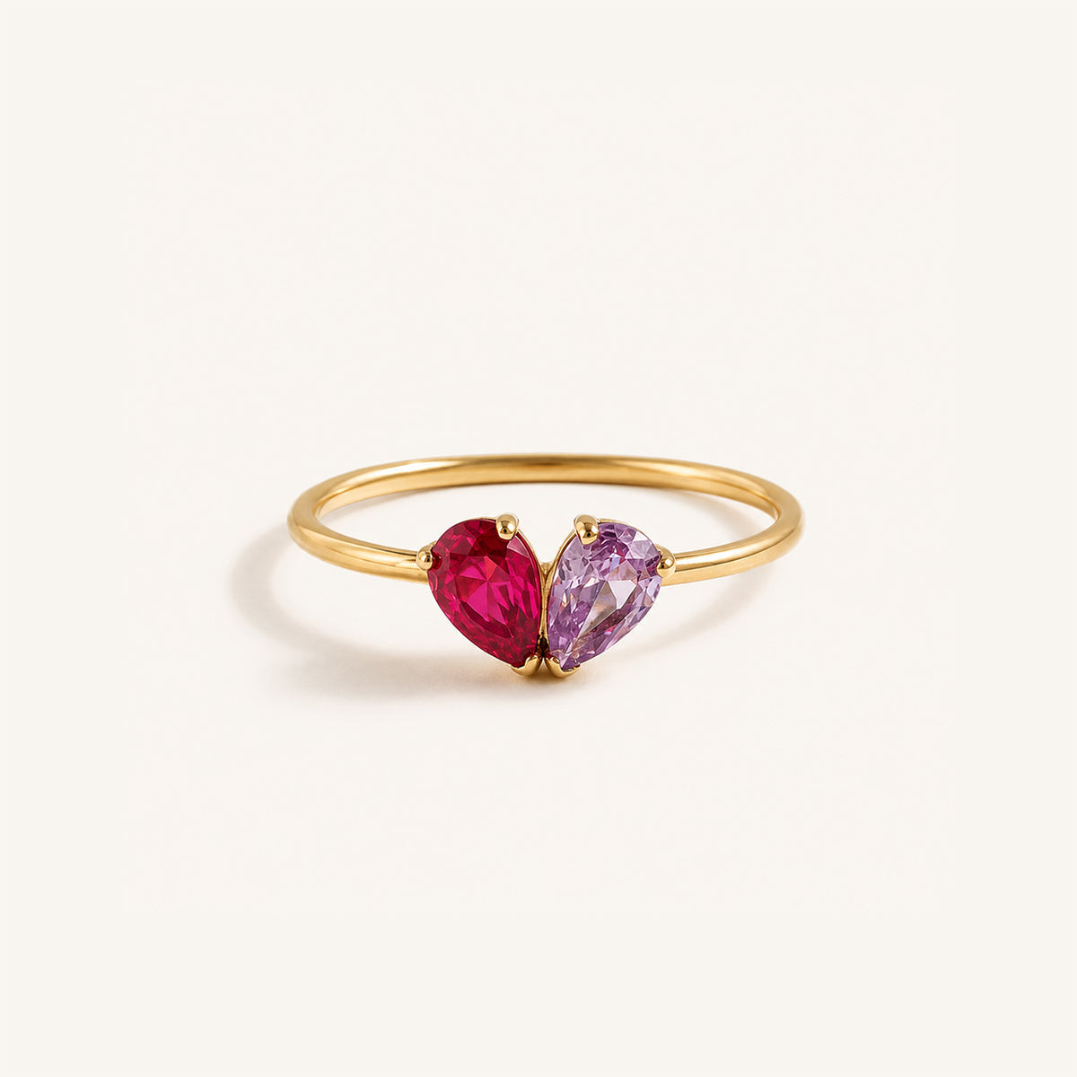 Toi et moi teardrop birthstone ring in 18K gold with ruby and amethyst pear stones forming a heart on cream background