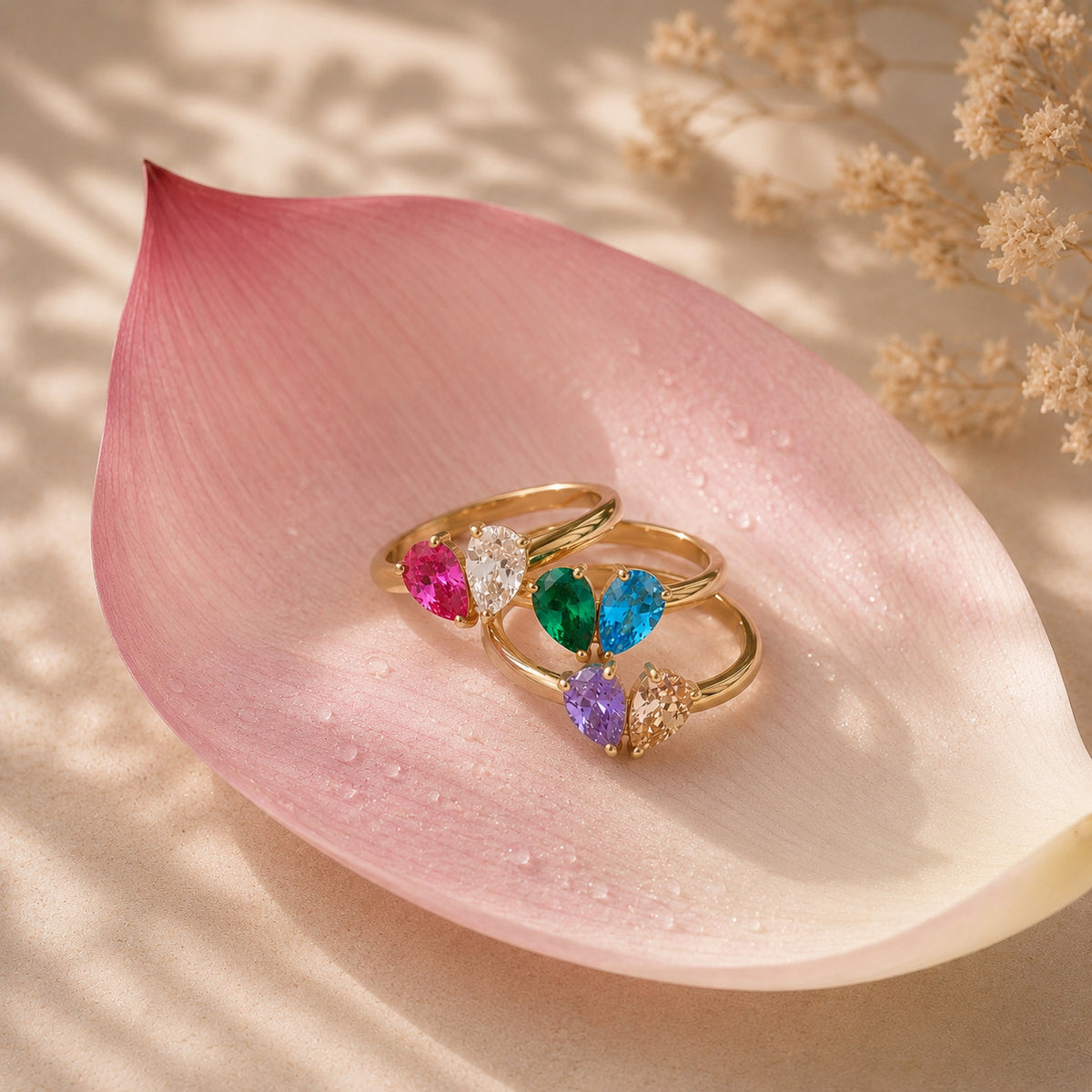 Gold toi et moi teardrop birthstone rings stacked on a pink lotus petal still life