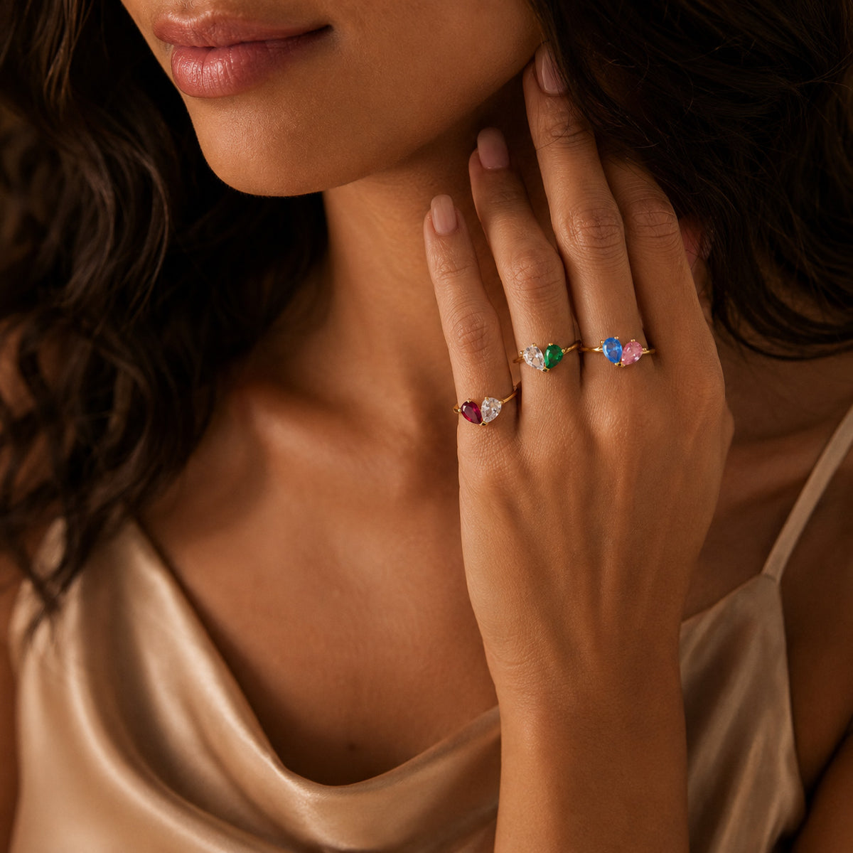 Woman wearing gold toi et moi teardrop birthstone ring, hand under chin