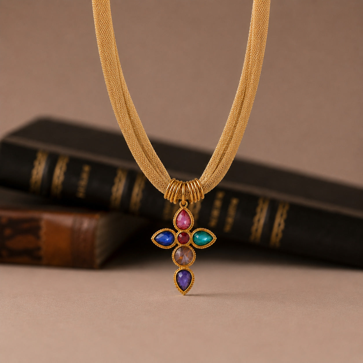 Vintage mesh rainbow cross necklace styled on cream still life with book
